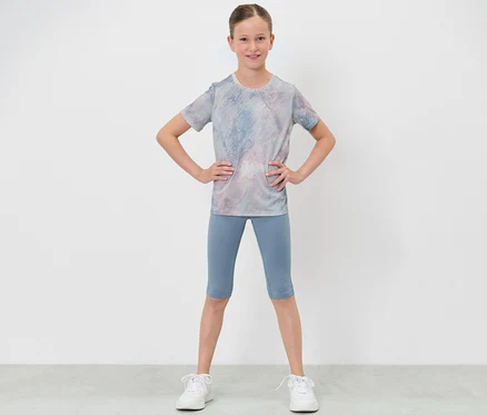 Mädchen in Sportkleidung posiert mit Händen in den Hüften, trägt eine Kinder-3/4-Sporttight und ein T-Shirt.