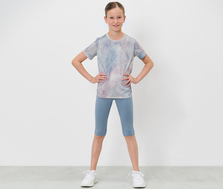 Mädchen in Sportkleidung posiert mit Händen in den Hüften, trägt eine Kinder-3/4-Sporttight und ein T-Shirt.