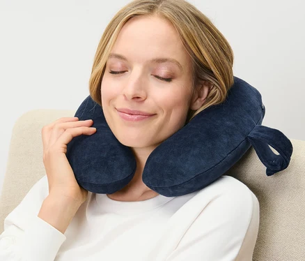 Frau sitzt mit blauem Nackenkissen, Memory Foam, im Sessel.