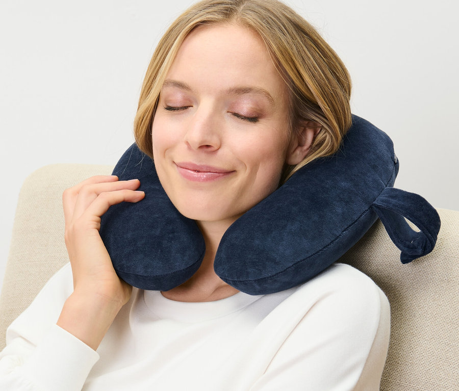 Frau sitzt mit blauem Nackenkissen, Memory Foam, im Sessel.