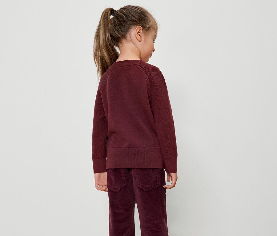 Mädchen mit Pferdeschwanz in bordeauxfarbenem Pullover und Samthose, von hinten.