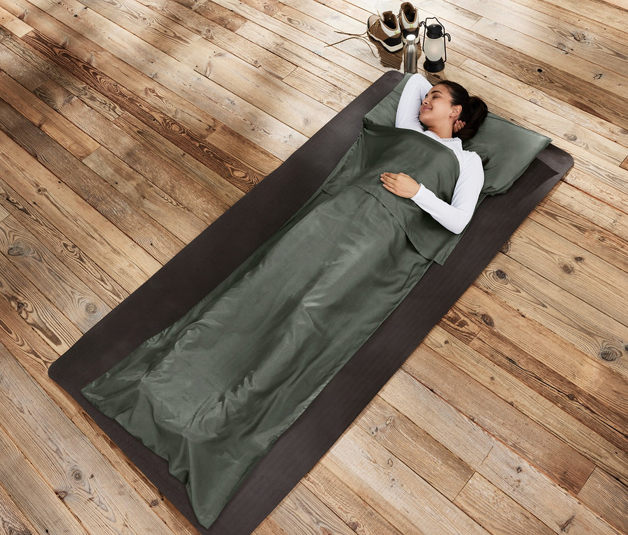 Frau liegt in Seiden-Schlafsack-Inlay auf einer Matte.