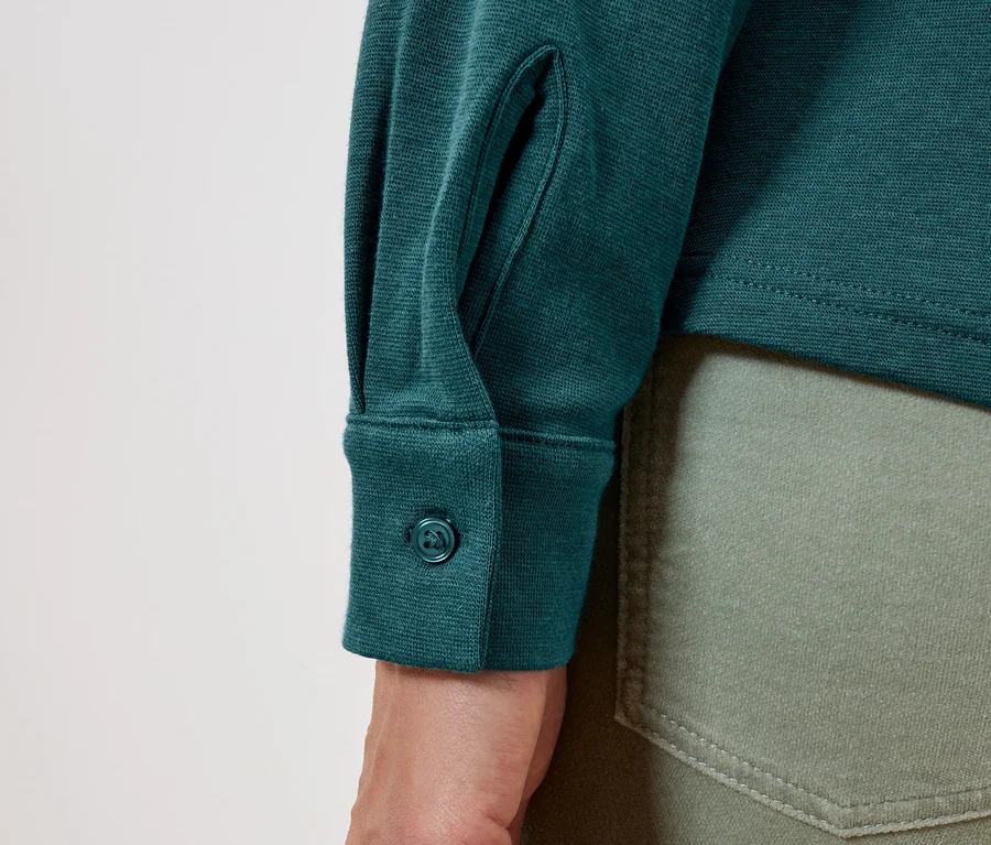 Detail eines grünen Langarmshirts mit Knopf an der Manschette und olivgrünen Jeans.