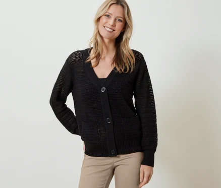 Frau trägt einen schwarzen Cardigan in Pointellestrick und eine beige Hose.
