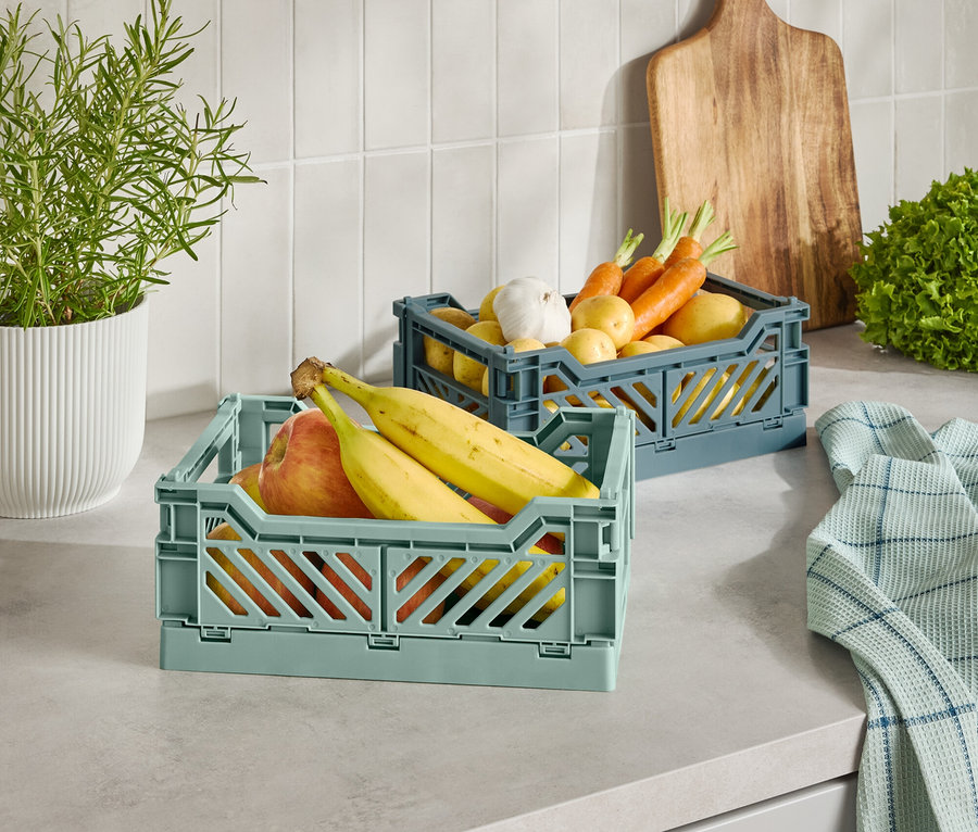 Zwei Kunststoffkörbe mit Obst und Gemüse auf einer Küchentheke.