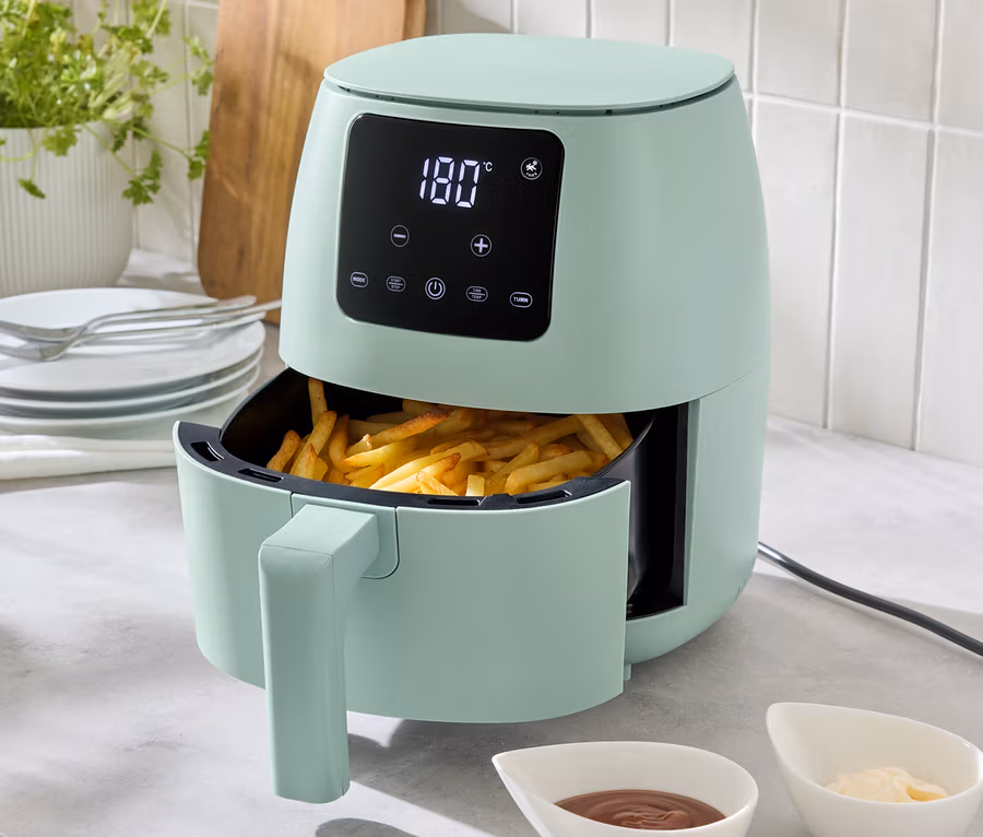 Eine hellgrüne Heißluft-Fritteuse, 2 l, steht auf einer Küchentheke, gefüllt mit Pommes Frites. Zwei Schälchen mit Soßen stehen davor.