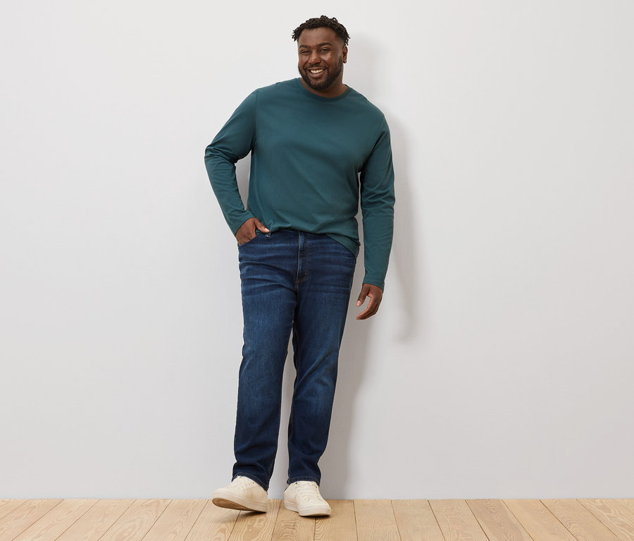 Mann posiert in einem grünen Langarmshirt und Jeans. Er trägt 2 Langarmshirts.