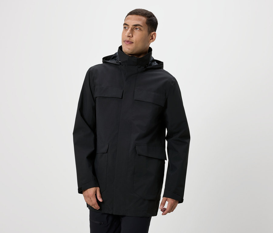 Mann posiert in einer schwarzen Jacke mit Kapuze und Taschen.