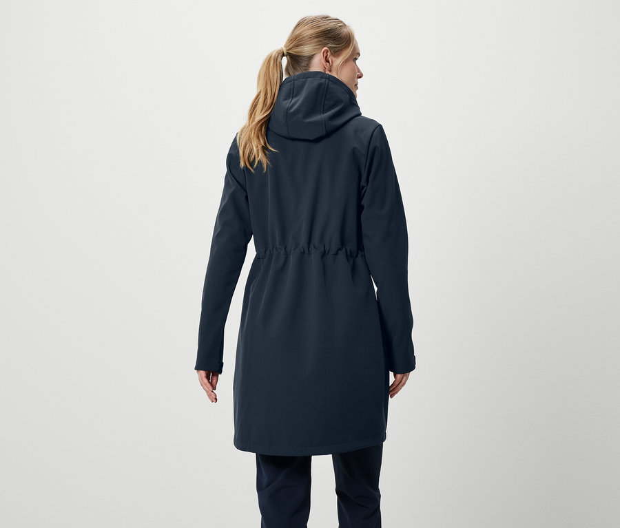 Rückansicht einer Frau mit blonden, zu einem Pferdeschwanz gebundenen Haaren, die einen dunkelblauen Mantel und eine Hose trägt.