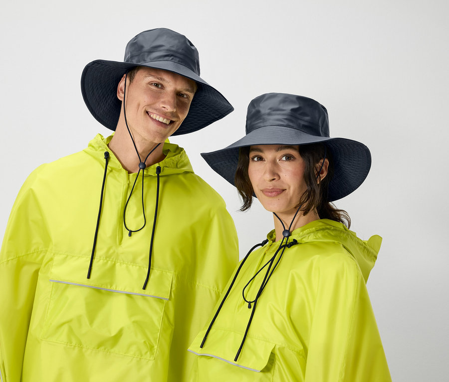 Ein Mann und eine Frau posieren in passenden gelben Regenjacken und grauen Hüten.