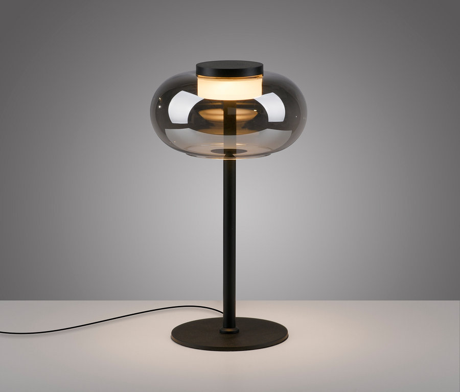 Eine schwarze Lampe mit einem birnenförmigen Glasschirm steht auf einem weißen Tisch.