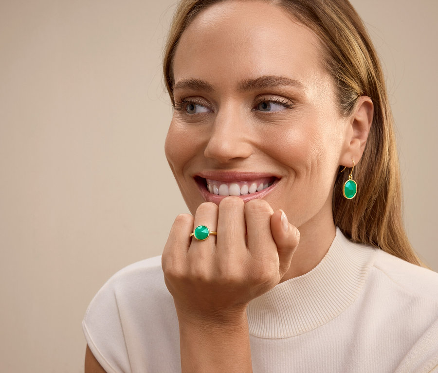 Lächelnde Frau mit Ring mit grünem Stein am Ringfinger und baumelnden Ohrringen mit grünem Stein.