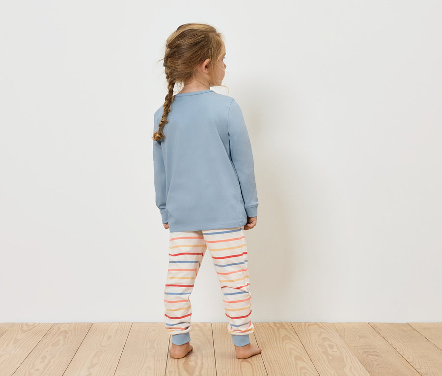 Mädchen in blauem Oberteil und gestreiften Hosen steht mit dem Rücken zur Kamera.