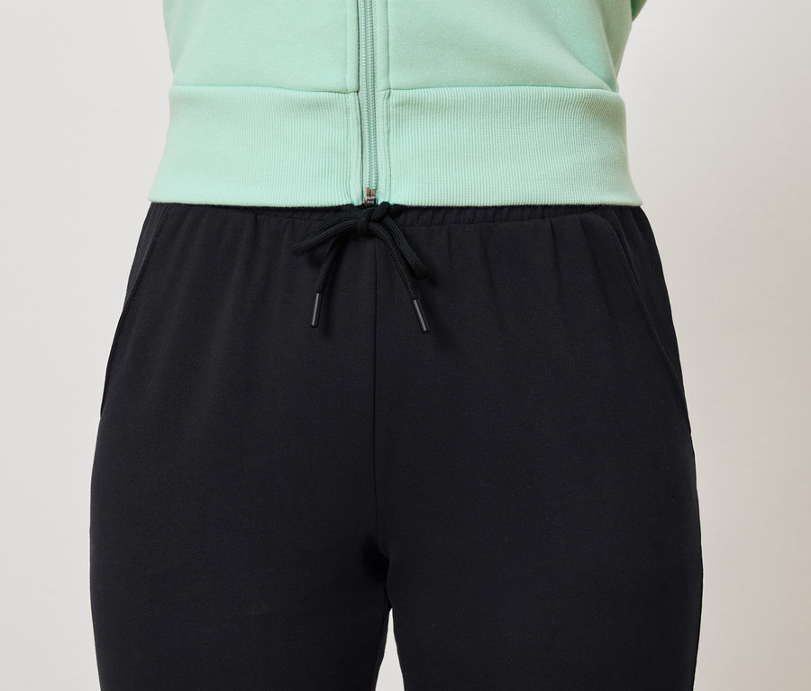 Schwarze Trainingshose mit Kordelzug und hellgrüne Jacke.