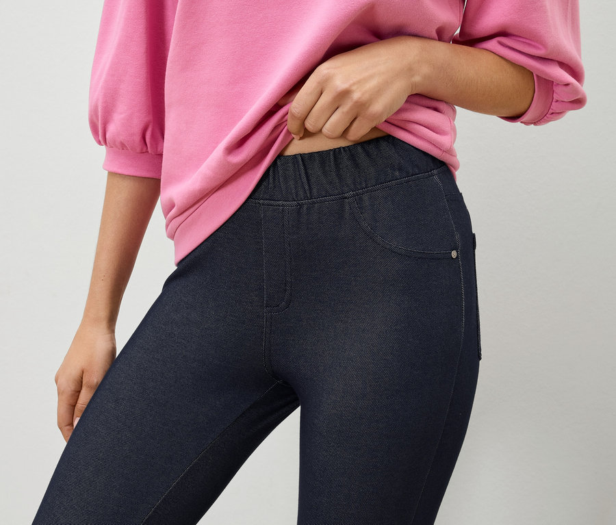 Frau hält ein pinkes Sweatshirt über dunkelblauen Jeggings.