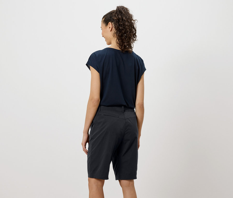 Rückansicht einer Frau mit lockigem Haar, die ein marineblaues T-Shirt und Shorts trägt.