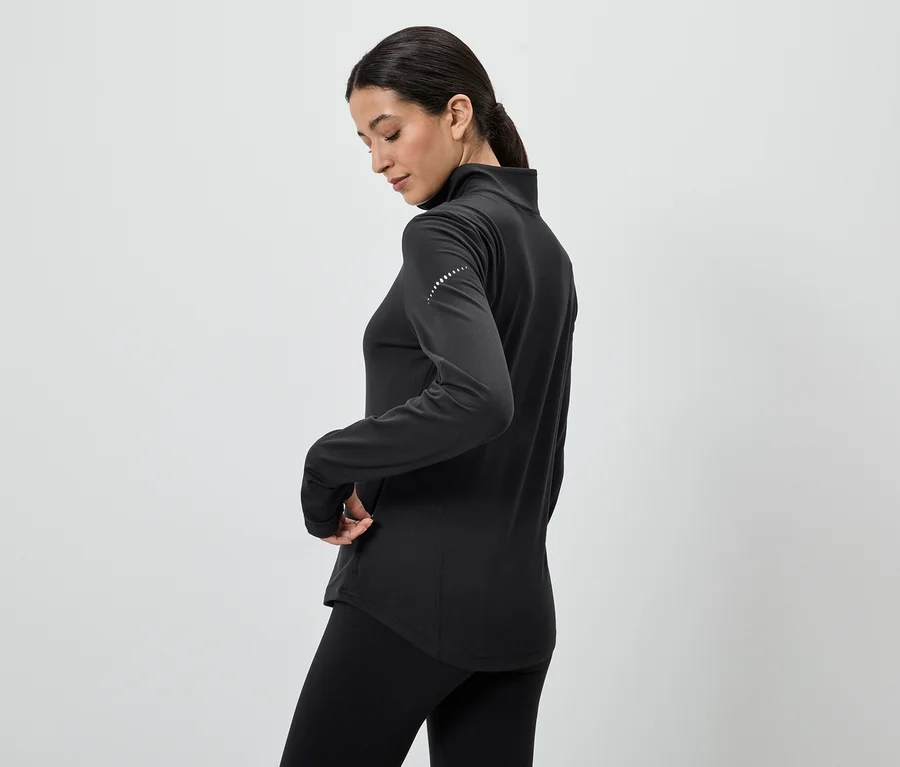 Frau in schwarzem Sportoberteil mit Reißverschluss und Leggings, Hand in der Tasche.