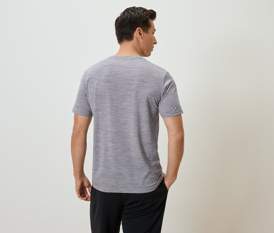 Mann von hinten, trägt ein meliertes, graues T-Shirt und schwarze Hosen.