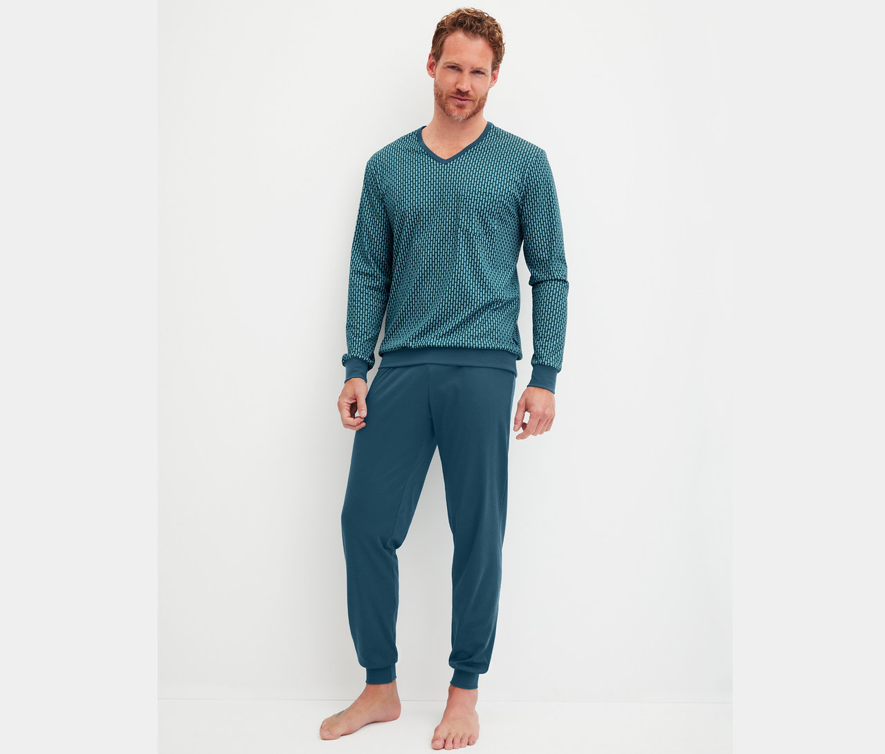 Ein Mann steht barfuß vor einer weißen Wand und trägt einen dunkelblauen Pyjama.