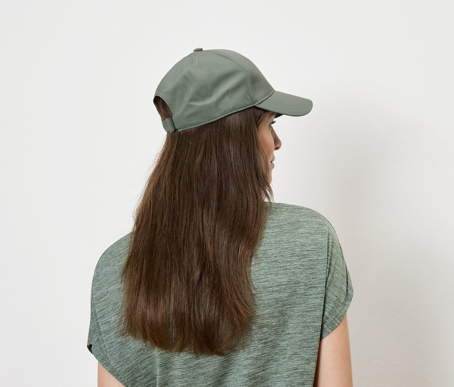 Rückansicht einer Frau mit langen braunen Haaren, die ein grünes Oberteil und eine grüne Kappe trägt.