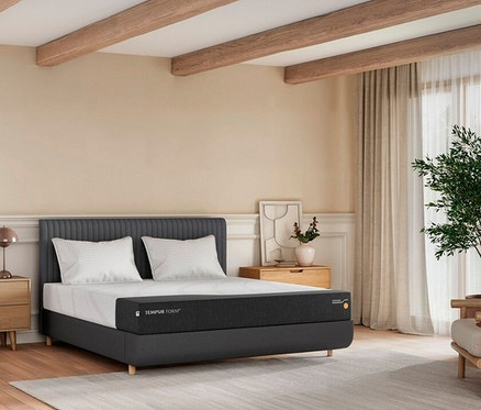Schlafzimmer mit einem grauen Bett mit Matratze und zwei Kissen. Auf beiden Seiten des Bettes stehen Nachttische.