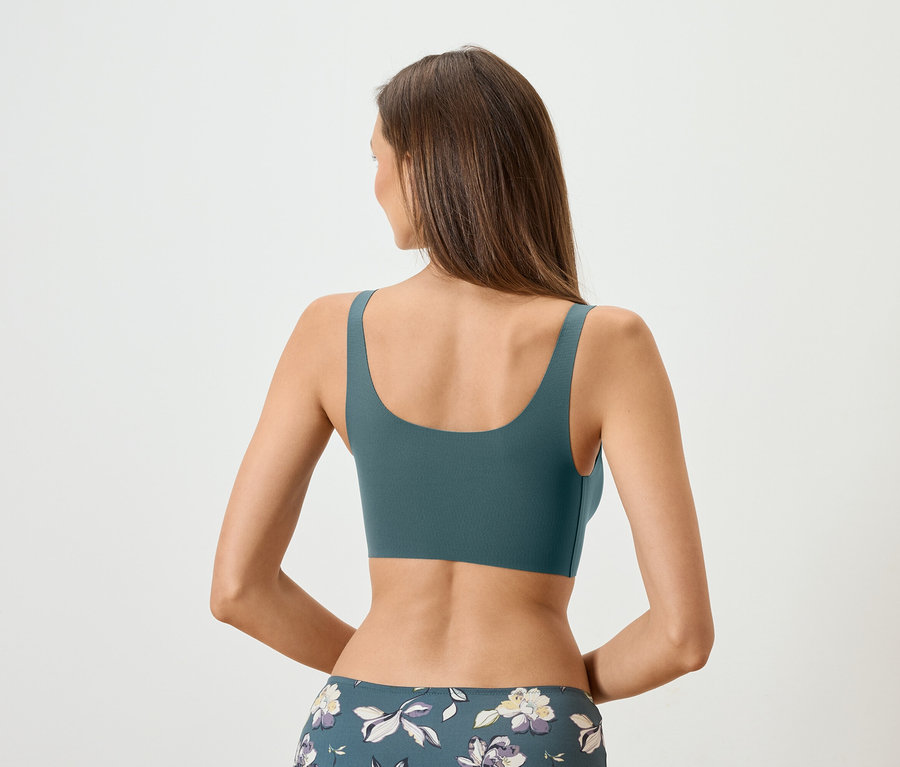 Rückansicht einer Frau mit langen braunen Haaren, die einen petrolfarbenen Sport-BH und blumige Leggings trägt.