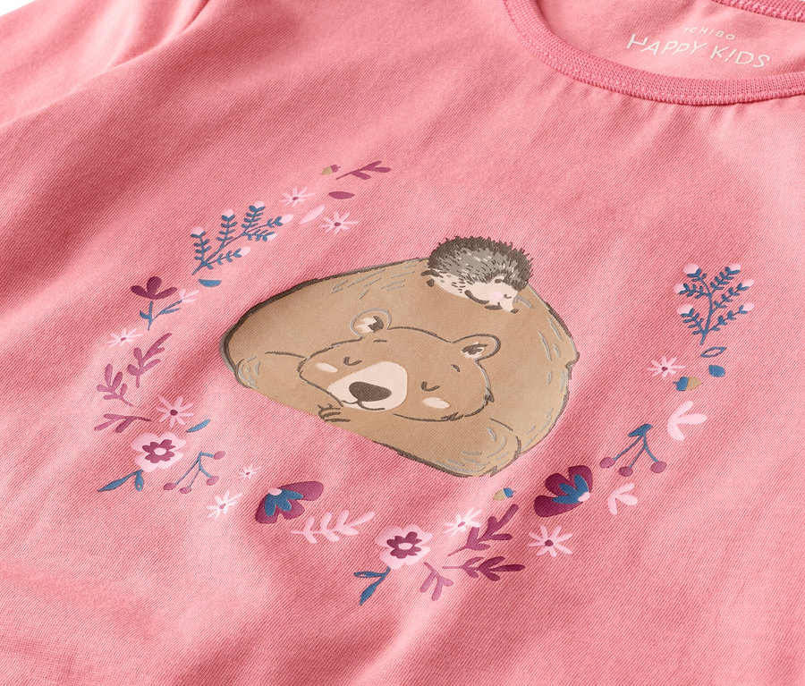 Auf einem rosafarbenen Shirt ist ein schlafender Bär mit einem Igel auf dem Rücken, umgeben von Blumen, abgebildet.