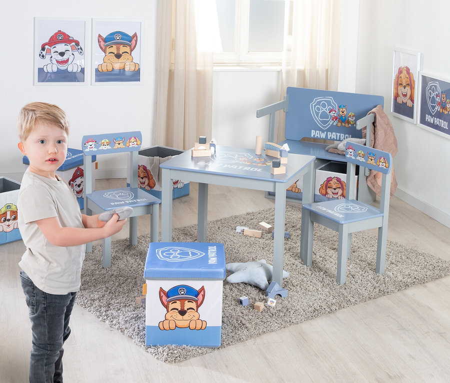 Ein kleiner Junge steht in einem Raum mit einem Tisch, Stühlen und einer Bank mit Paw Patrol Motiven.