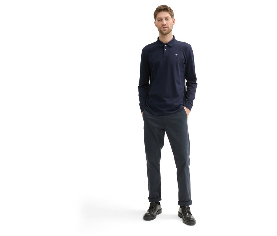 Mann in Tom Tailor Longsleeve Piqué Poloshirt, Sky Captain Blue, und dunkler Hose mit schwarzen Schuhen.