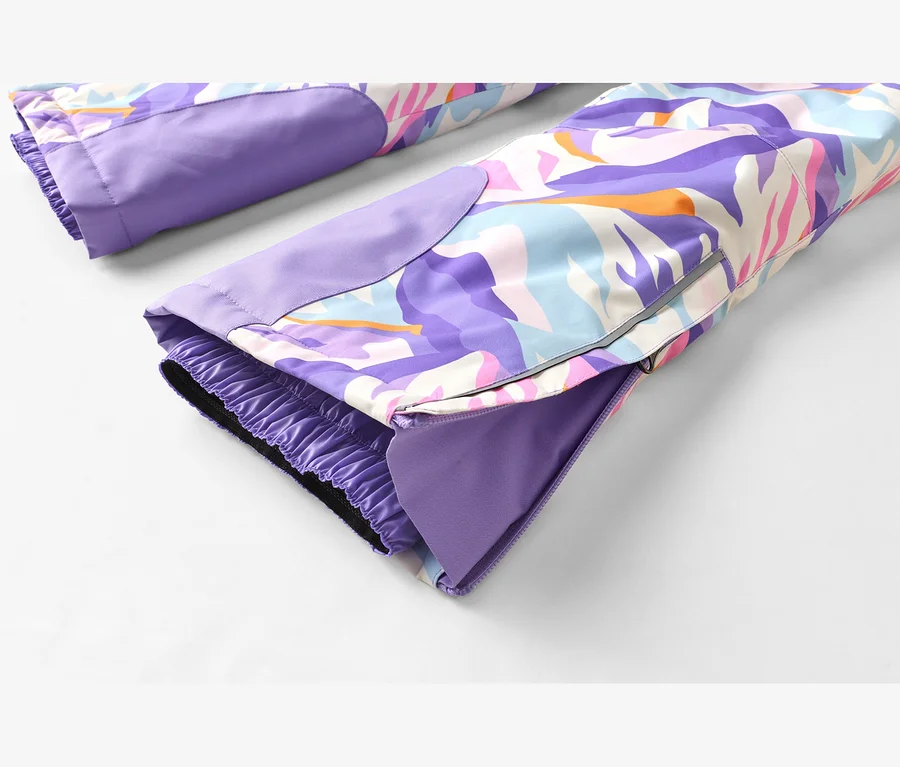 Nahaufnahme der Unterschenkel einer Skihose mit buntem, abstraktem Muster in Lila, Blau, Pink, Orange und Weiß. Die Beinöffnungen haben elastische Innenbündchen und Reißverschlüsse, die ein lila Futter zeigen.