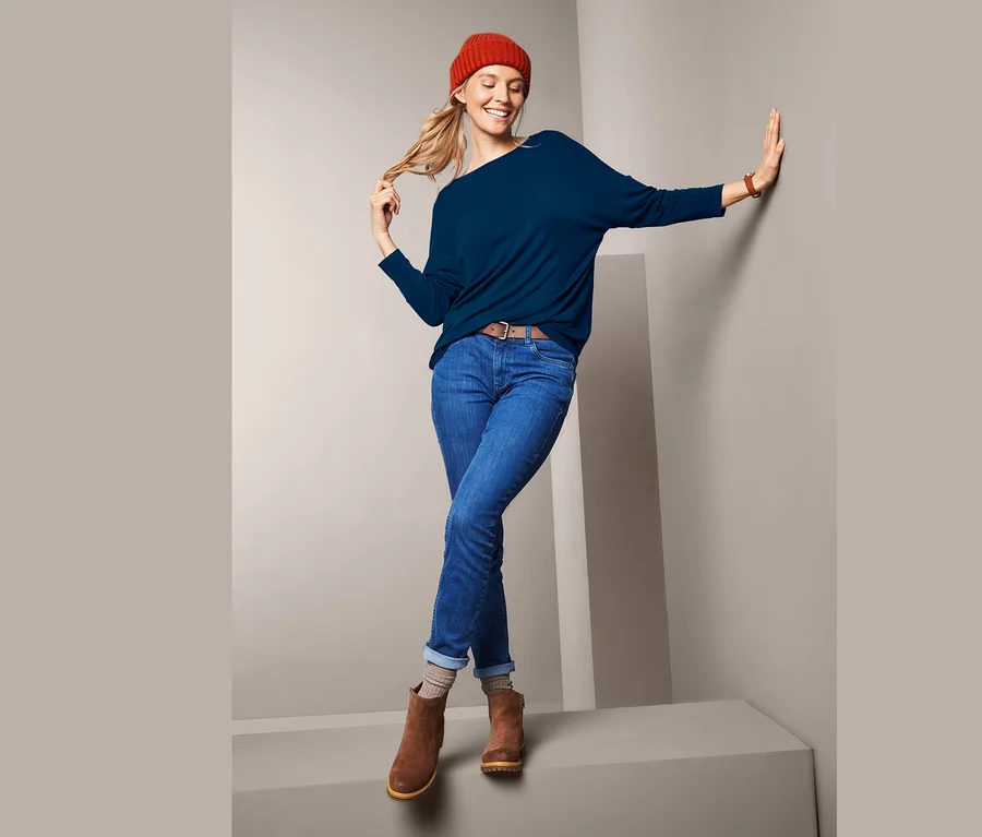 Frau posiert in blauem Oversized-Shirt, Jeans und braunen Stiefeln.