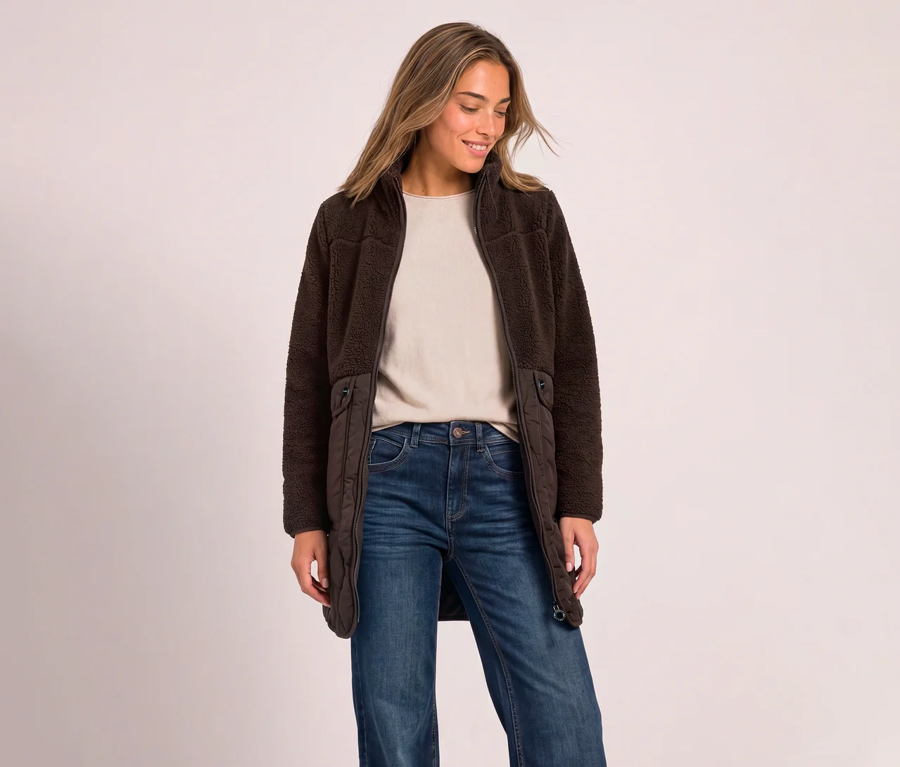 Eine Frau trägt einen offenen Street One Teddymantel in Dunkelbraun über einem beigen Oberteil und blauen Jeans.