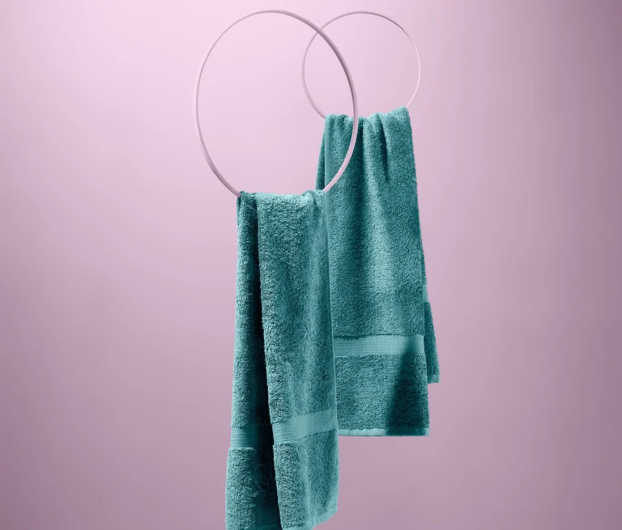 Zwei blaugrüne Frottier-Handtücher, 2 Stück, hängen an weißen Ringen vor einem rosa Hintergrund.