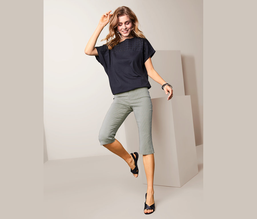 Frau posiert in gestreifter Stretchhose in 3/4-Länge und schwarzem Oberteil.