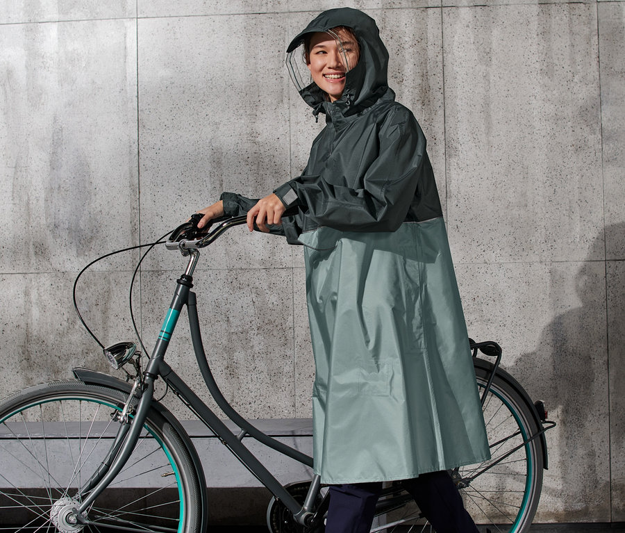 Eine Frau in einem Unisex-Regenponcho mit Ärmeln schiebt ein Fahrrad.