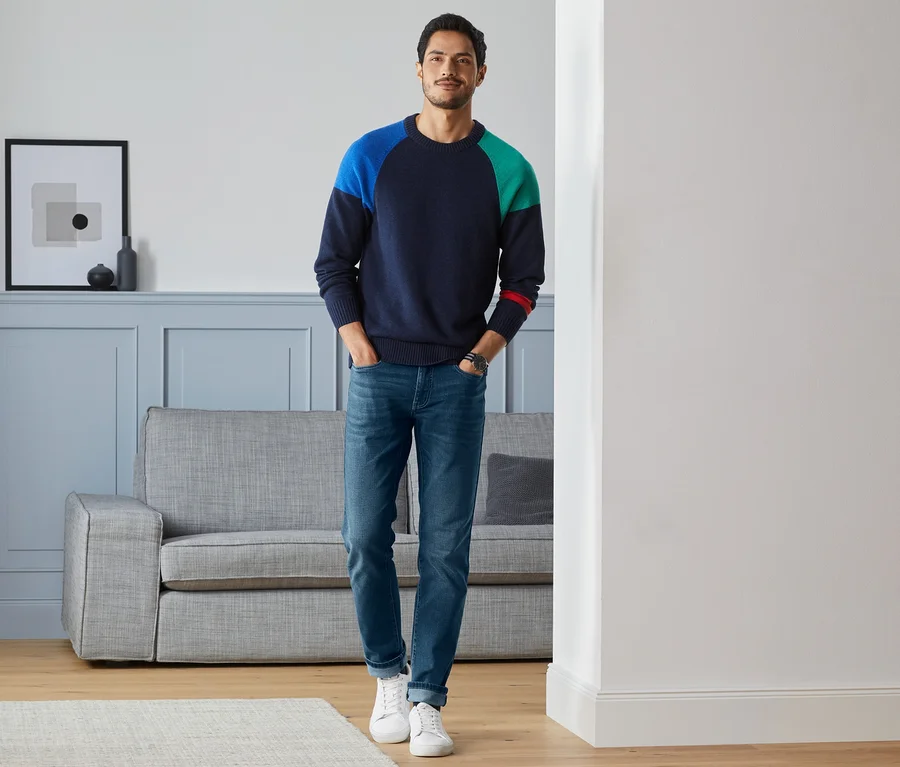 Mann steht im Wohnzimmer und trägt eine Jeans im Five-Pocket-Style.