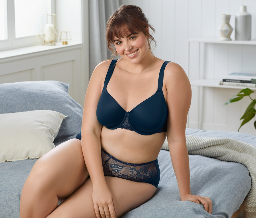 Frau sitzt auf einem Bett und trägt einen dunkelblauen Bügel-BH.