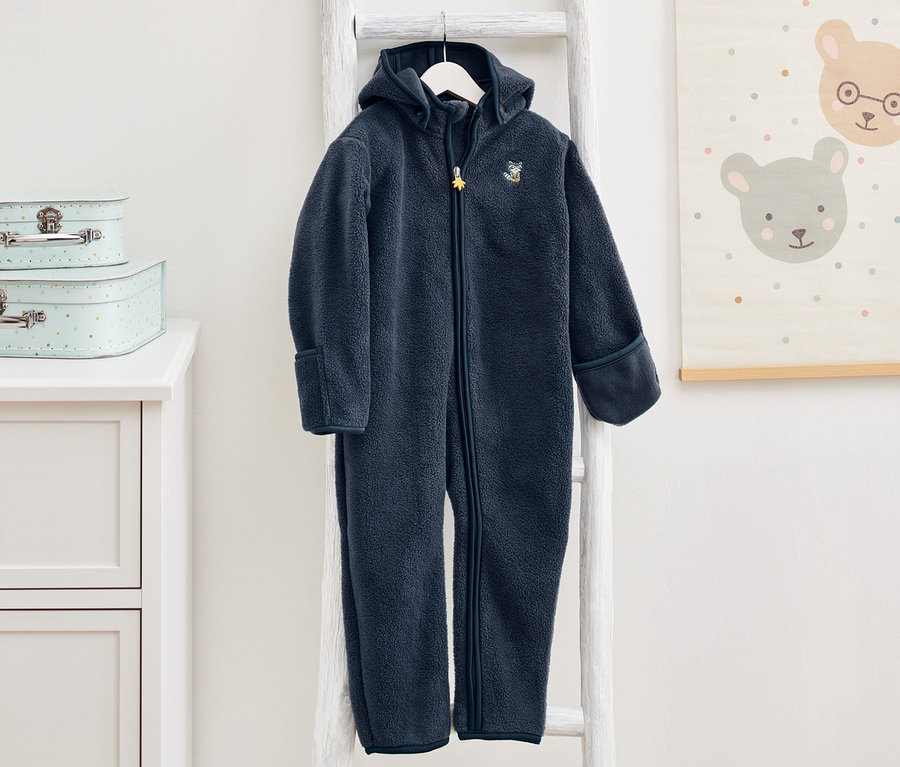 Dunkelblauer Fleece-Einteiler hängt auf einer weißen Leiter im Kinderzimmer.
