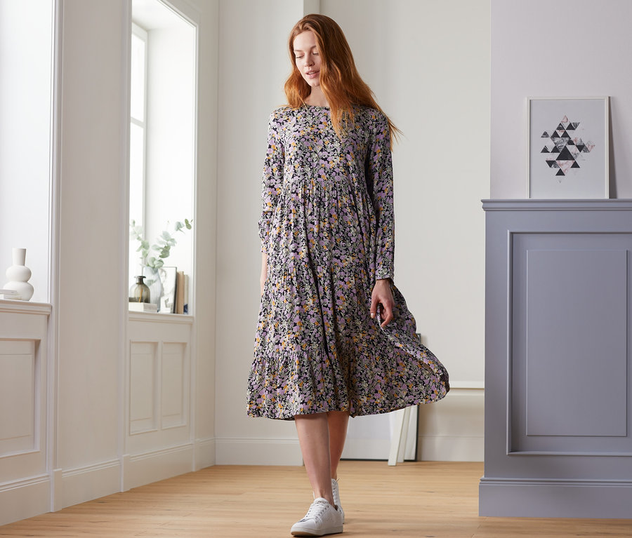 Frau geht in einem geblümten Midikleid über den Boden.