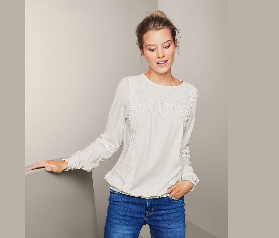 Frau posiert in einem Blusenshirt mit Stickerei und Jeans.