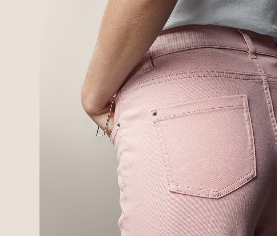 Detailansicht einer Frau, die eine roséfarbene Slimfit-Jeans trägt und eine Hand in der Tasche hat.