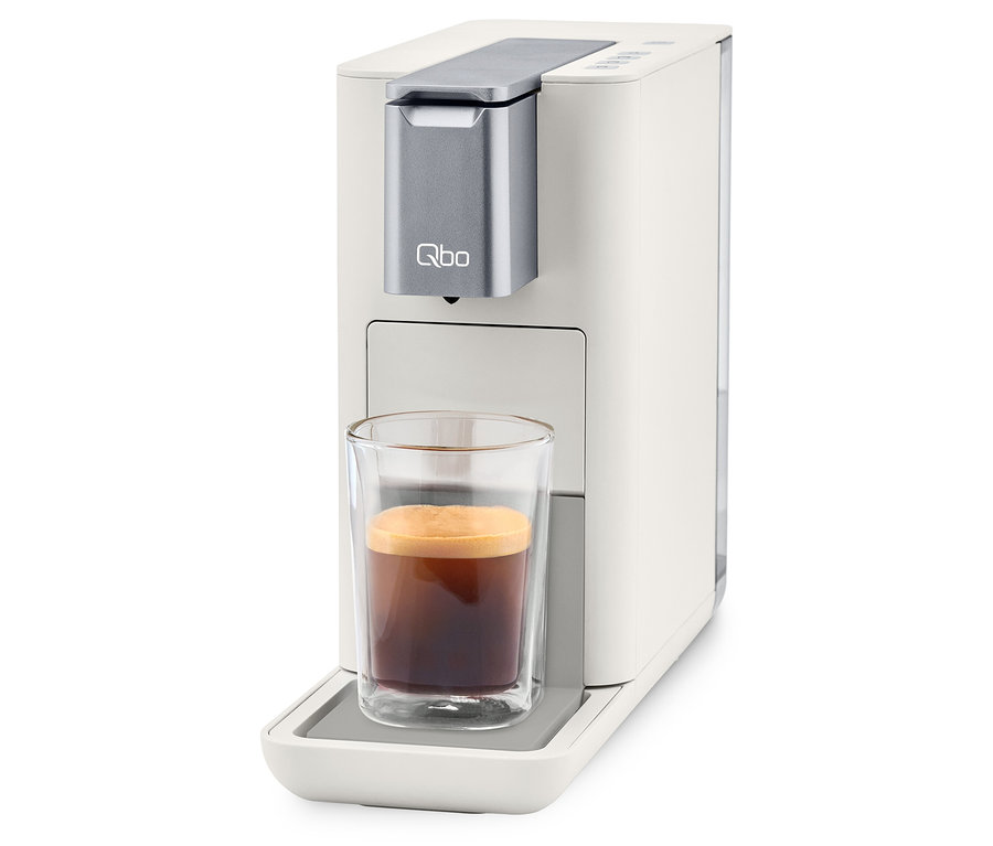 Qbo ESSENTIAL Bright Sand Kaffeemaschine mit Tasse Kaffee.
