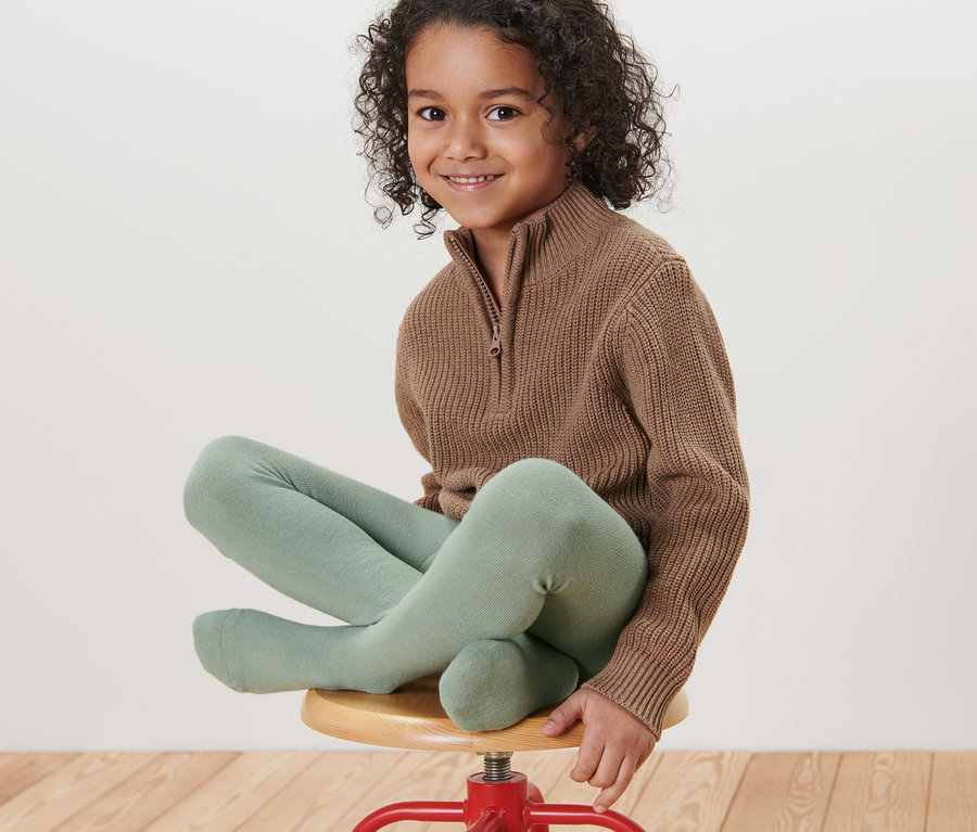 Ein Mädchen sitzt auf einem roten Hocker und trägt hellgrüne Kinder-Strumpfhosen.