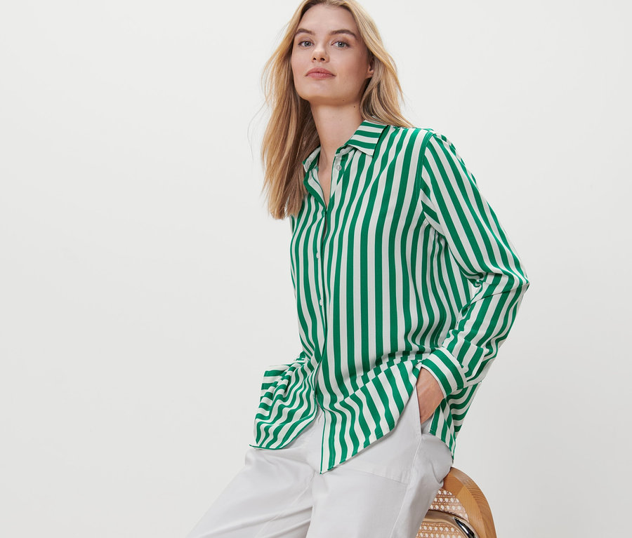 Blonde Frau sitzt auf einem Stuhl und trägt eine grüne gestreifte Bluse.