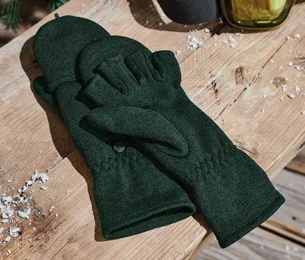 Grüne Strickfleece-Klappfäustlinge liegen auf einer Holzbank neben einer Skibrille.