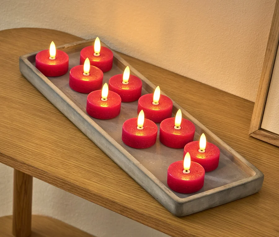 Zehn rote LED-Echtwachs-Teelichter liegen auf einem grauen Tablett auf einem Tisch.