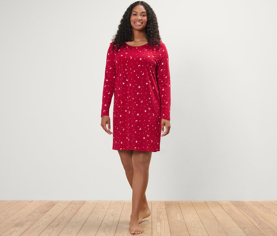 Eine Frau steht und lächelt in die Kamera, sie trägt ein rotes Nachthemd.