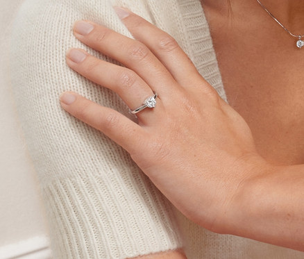 Porträt einer sitzenden Frau, die einen Solitärring aus 925er Silber mit Zirkonia und eine Halskette mit Zirkonia-Solitäranhänger trägt.
