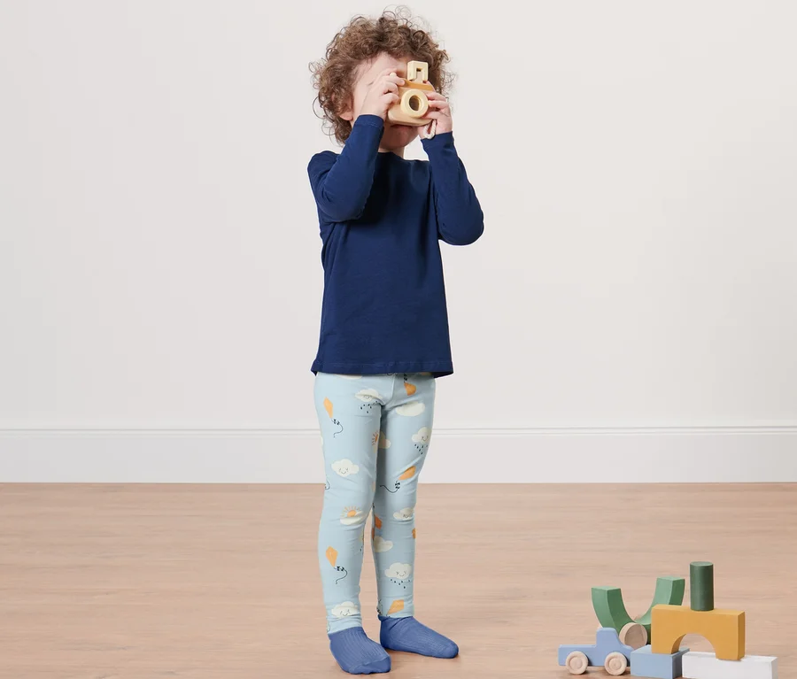 Ein Junge in blauem Oberteil und 2 Kleinkinder-Leggings spielt mit einer Holzkamera.