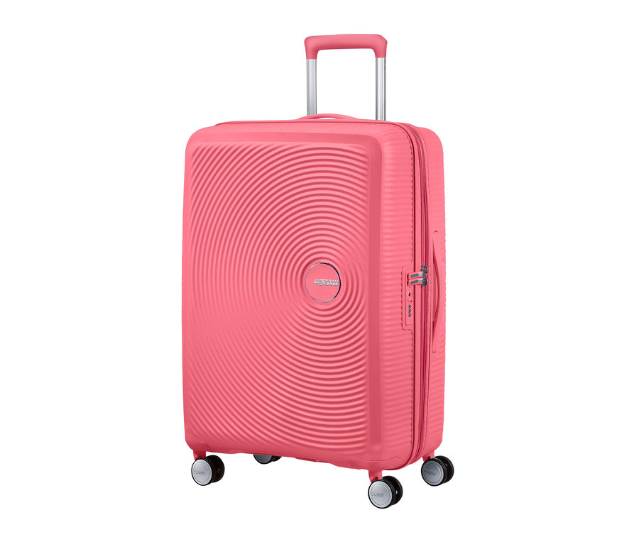 Nahaufnahme eines mittelgroßen, sonnengeküssten korallenroten American Tourister Hartschalenkoffers »Soundbox« Spinner.